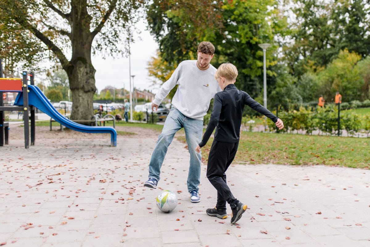 jongere en kind voetballen op schoolplein