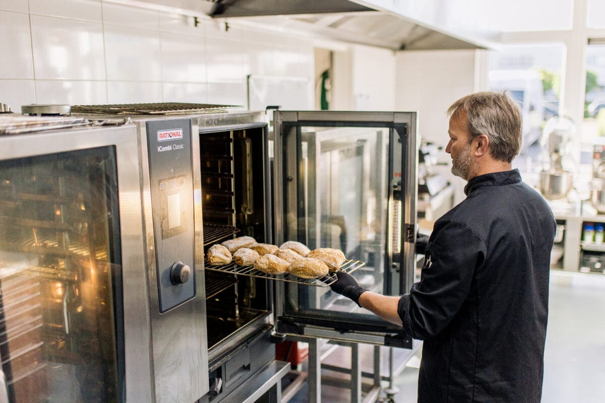 kok (ondernemer) die broodjes in de oven steekt.